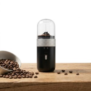 Molinillo de café eléctrico portátil negro con recipiente transparente y detalle plateado, junto a granos de café.
